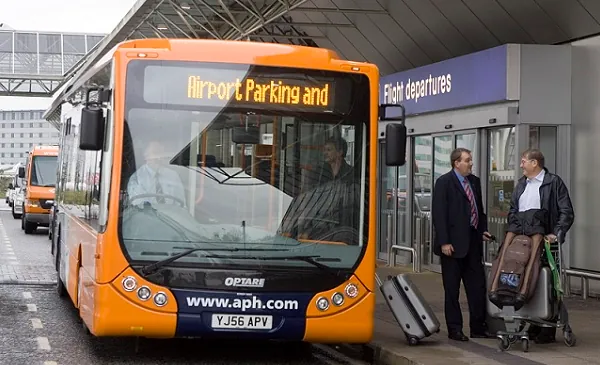 An airport parking shuttle bus picking passengers up outside a flight departures terminal